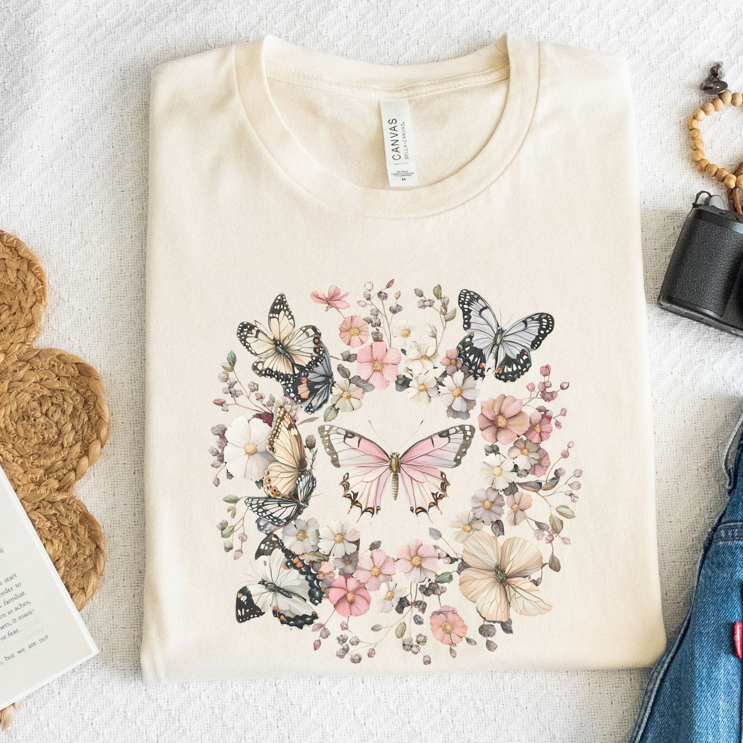 Beige t-shirt with butterfly and floral design on a textured surface