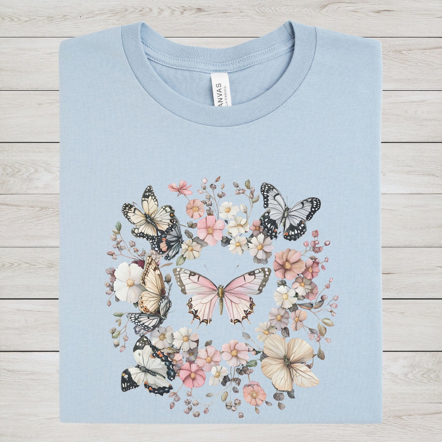 Light blue t-shirt with butterfly and floral design on a wooden surface