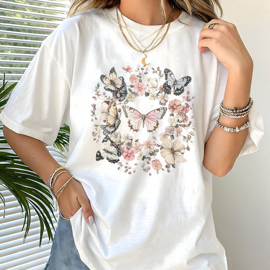 White t-shirt with butterfly design worn by a person, with a plant in the background