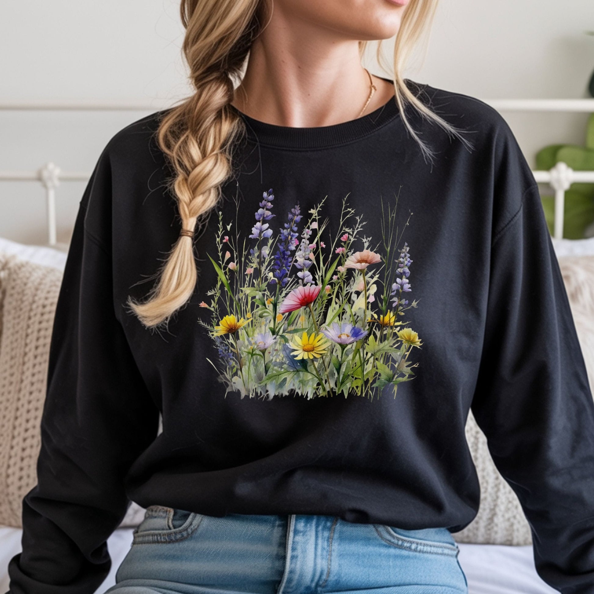 Person wearing a black long sleeve t-shirt with a floral design, sitting on a bed.
