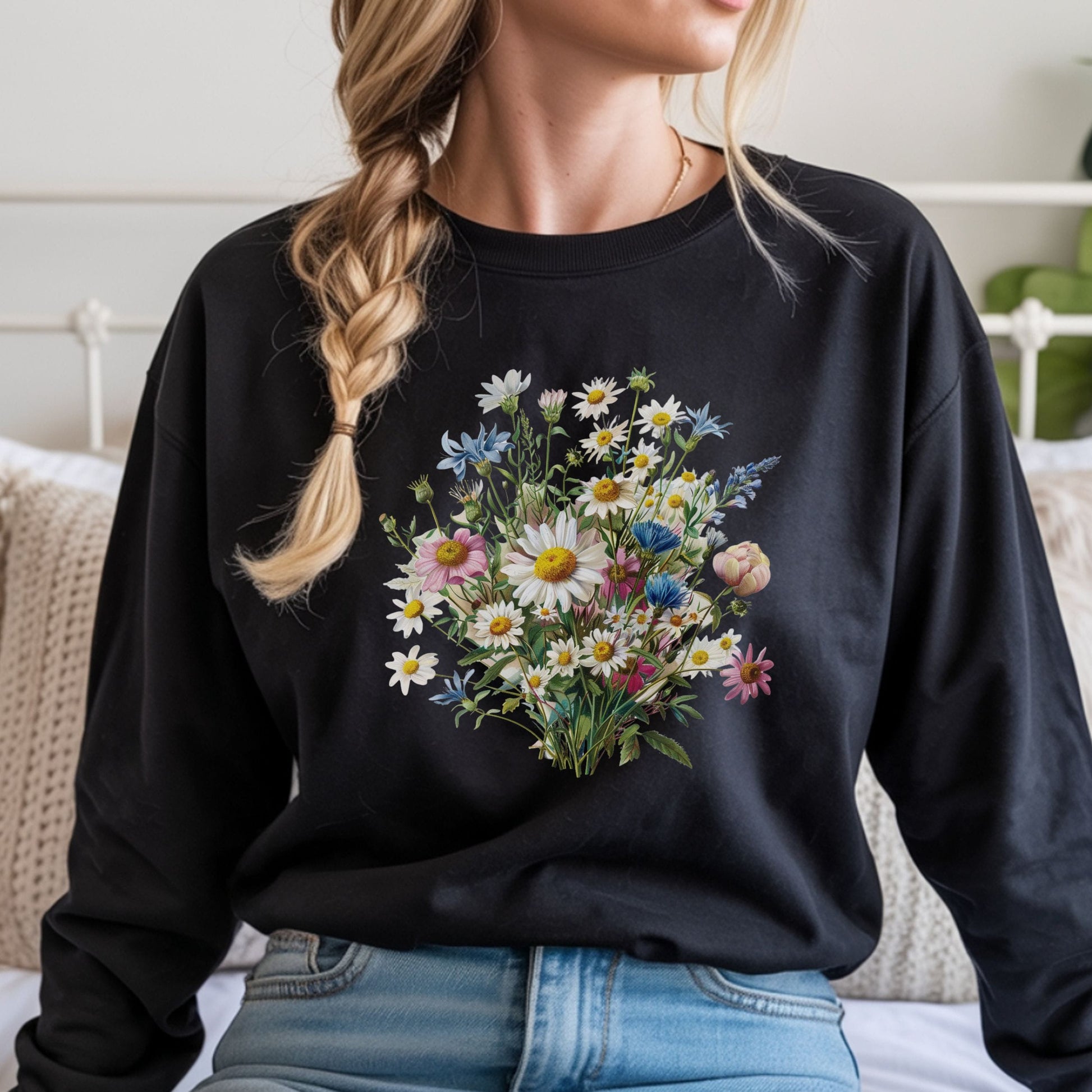Person wearing a black long sleeve t-shirt with a floral design, sitting on a bed.