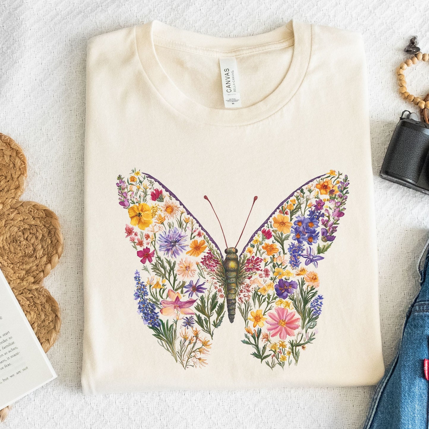 Beige t-shirt with a colorful butterfly design on a textured surface.