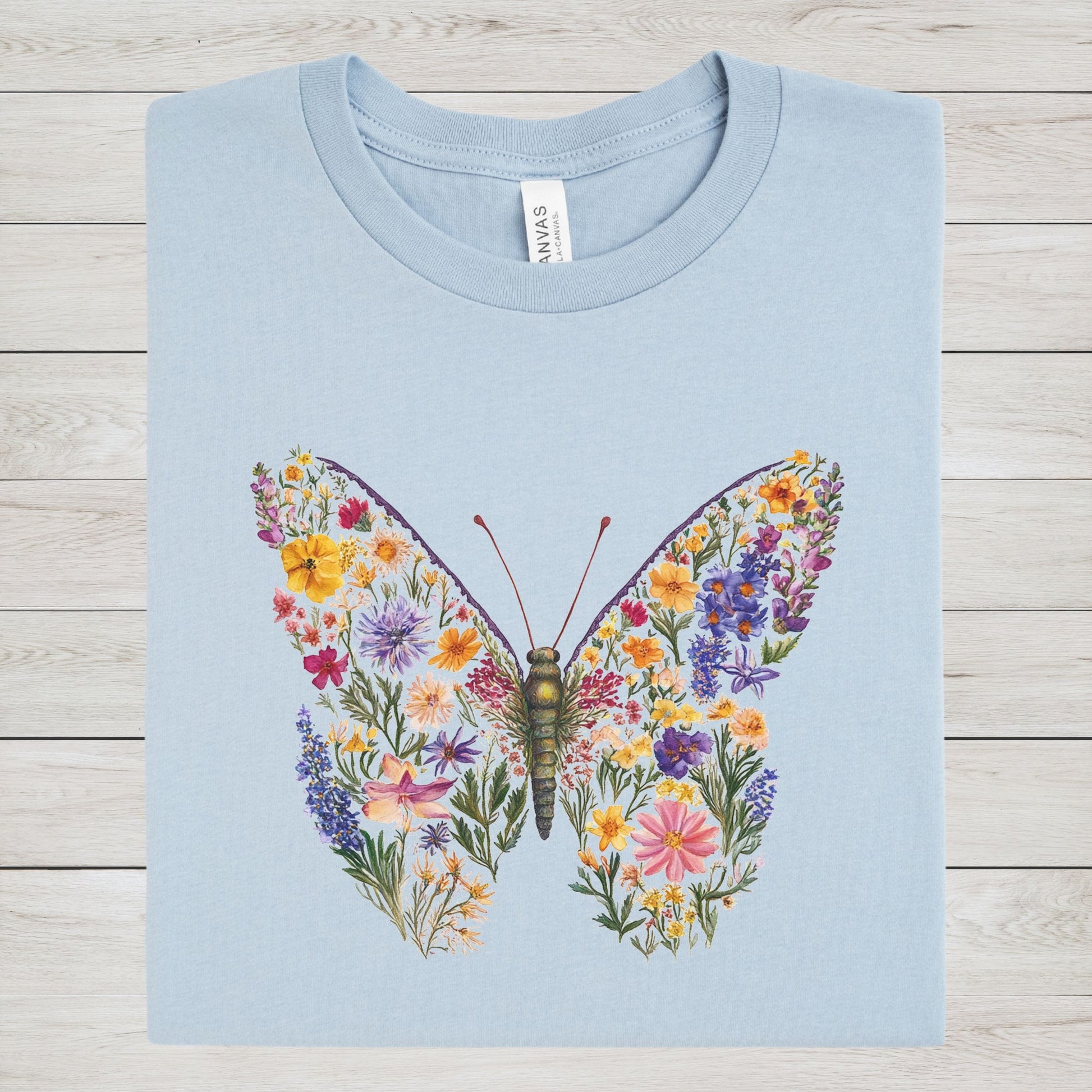 Light blue t-shirt with a colorful butterfly design on a wooden surface