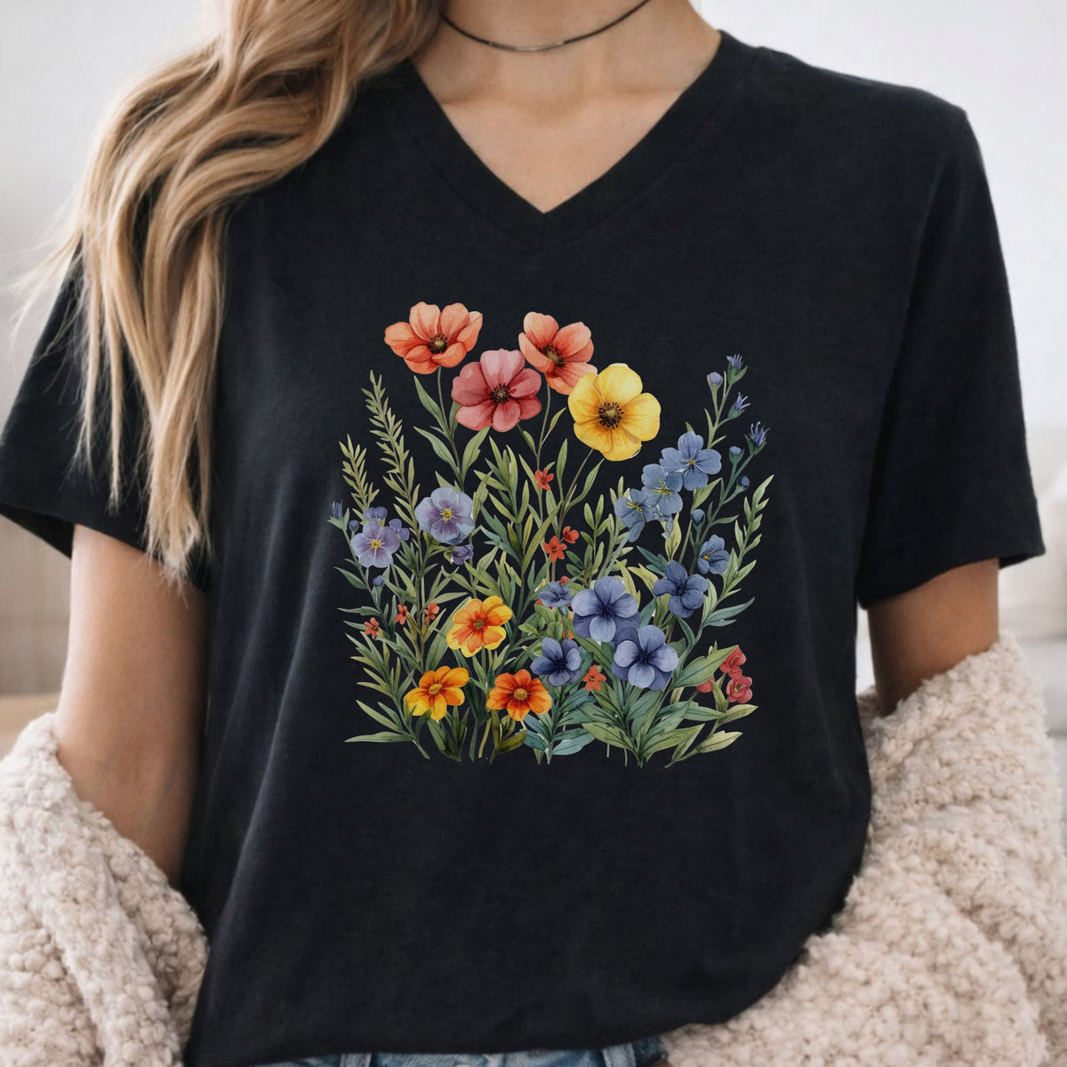 A woman wearing a black V-neck t-shirt with a colorful watercolor-style wildflower graphic on the front, paired with a beige fuzzy cardigan.