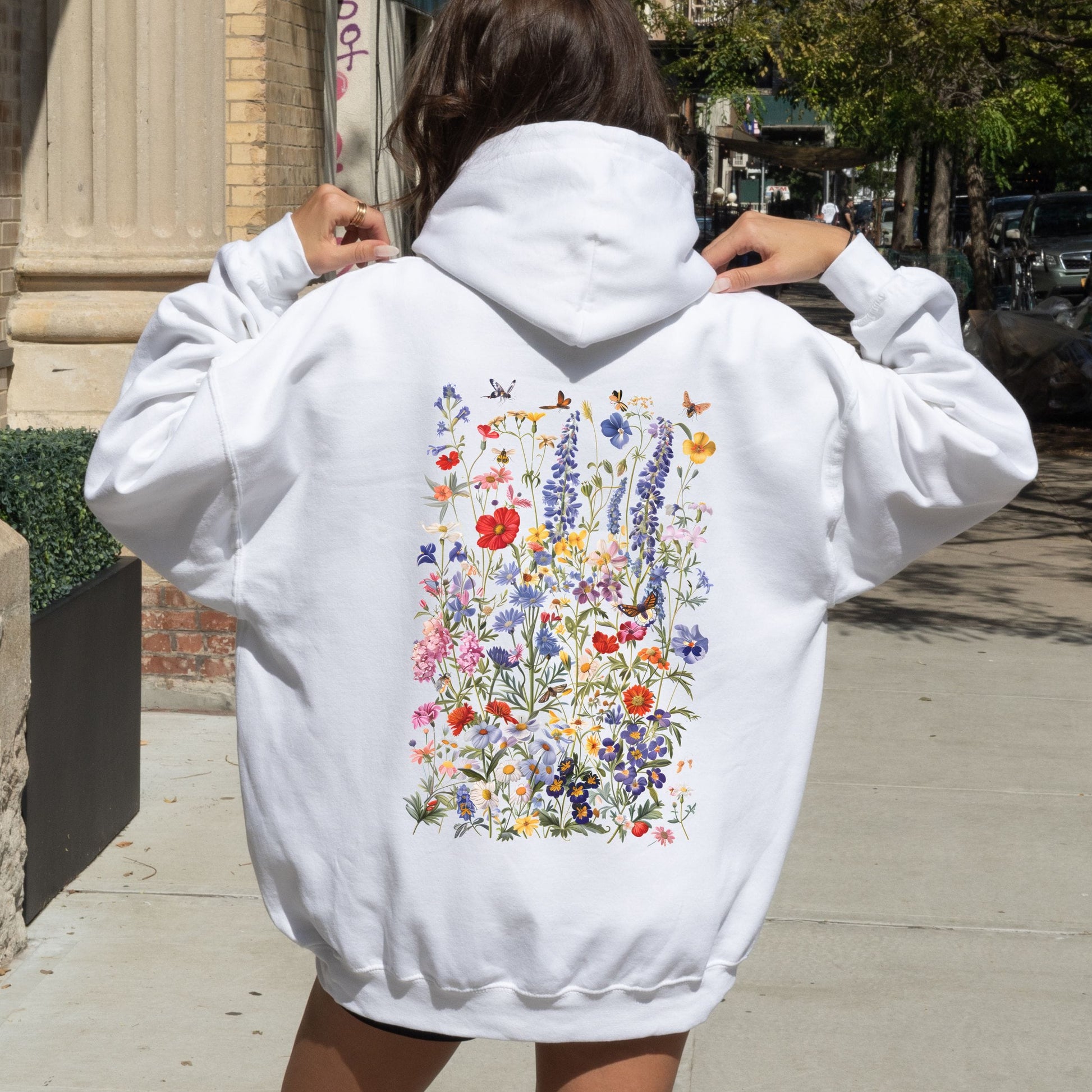 Person wearing a white hoodie with floral designs on the back, standing outdoors.
