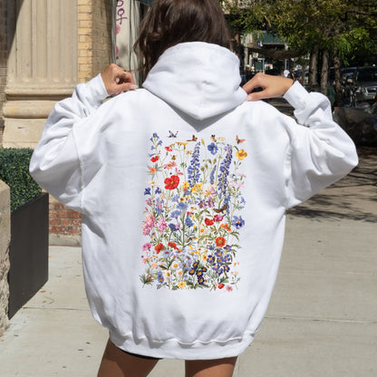 Person wearing a white hoodie with floral designs on the back, standing outdoors.