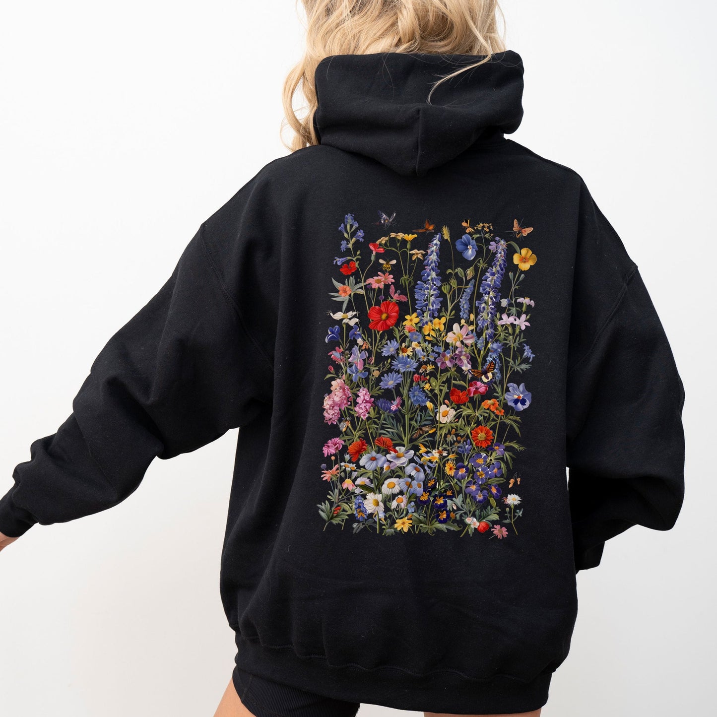 Person wearing a black hoodie with floral designs on the back against a white background