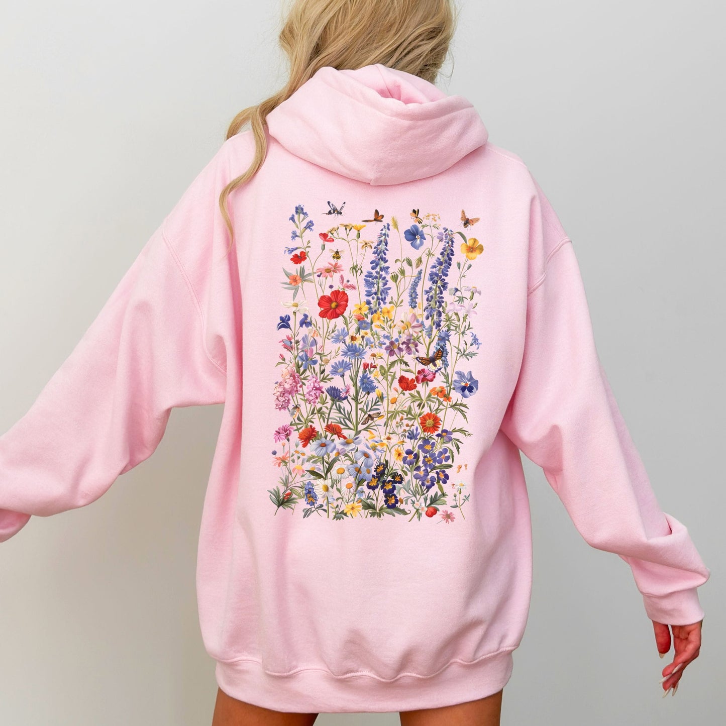 Pink hoodie with floral design on the back worn by a person against a plain background