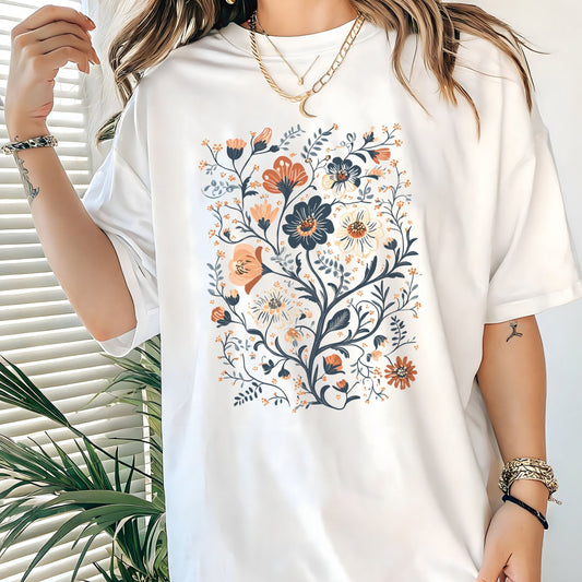 White t-shirt with floral design worn by a person, with a plant in the background