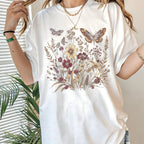 White t-shirt with floral and butterfly design worn by a person, with a plant in the background.