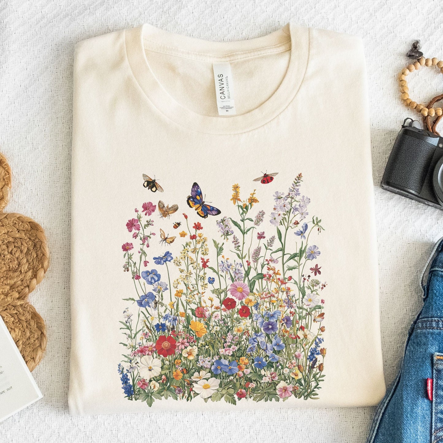 Flat lay of natural t-shirt featuring colorful wildflower meadow with butterflies