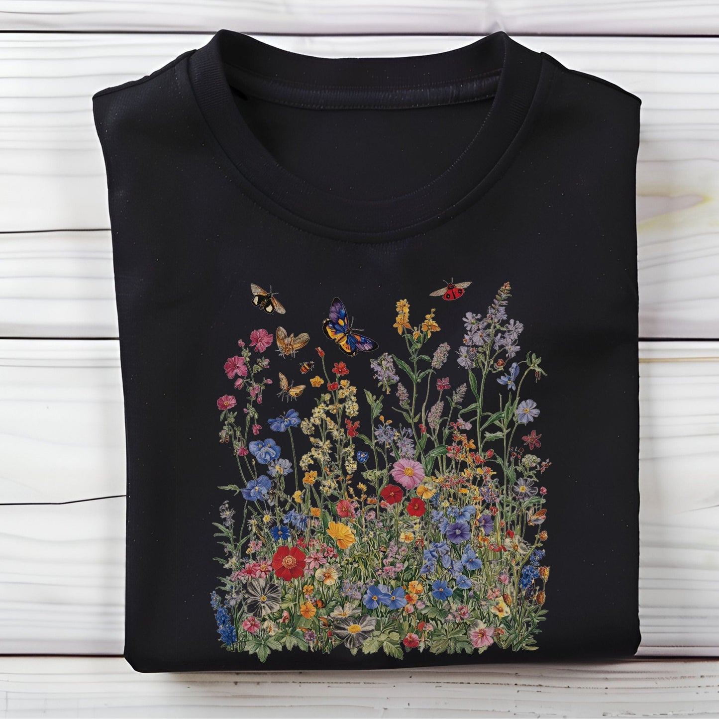 Flat lay of black t-shirt featuring colorful wildflower meadow with butterflies