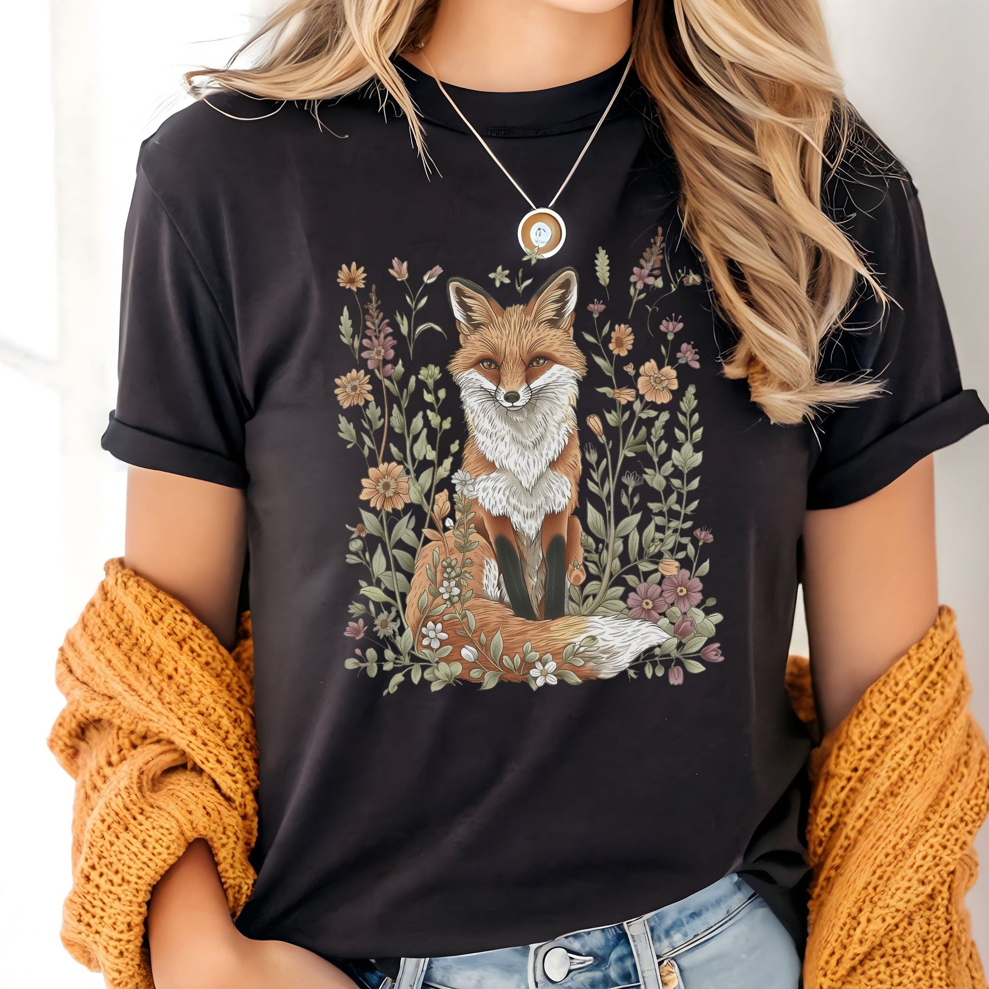 Person wearing a black t-shirt with a fox and floral design, holding a yellow knitted item.