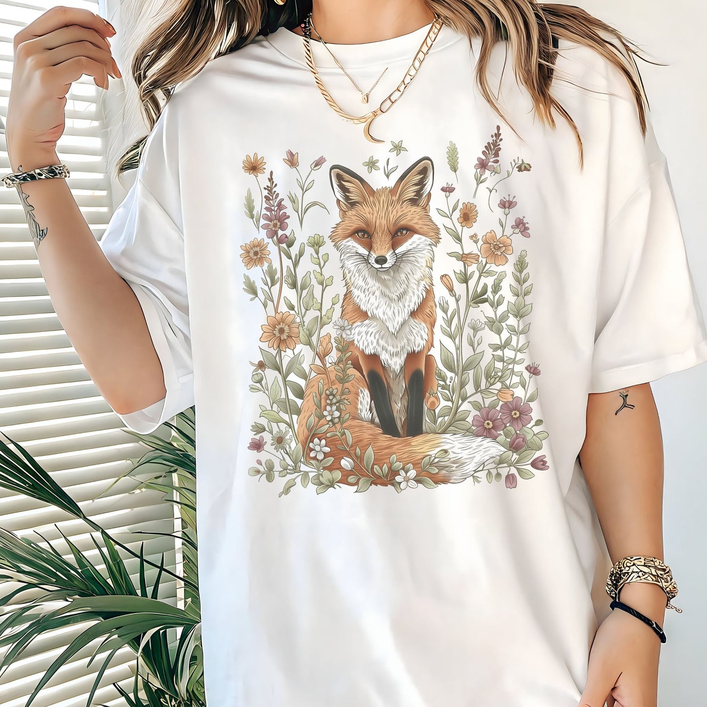 White t-shirt with a fox and floral design worn by a person, with a plant in the background.